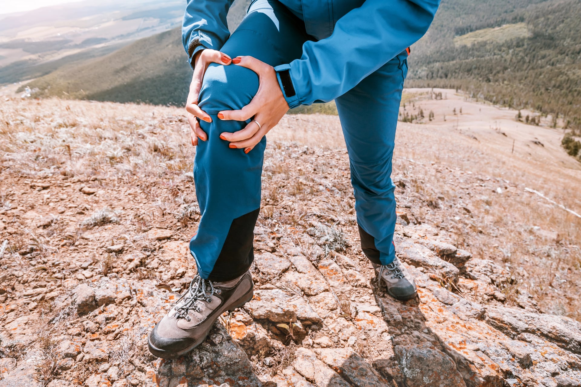 Woman is holding on to the knee joint, suffering from acute pain. Concept of injury of meniscus during a hike in the highlands