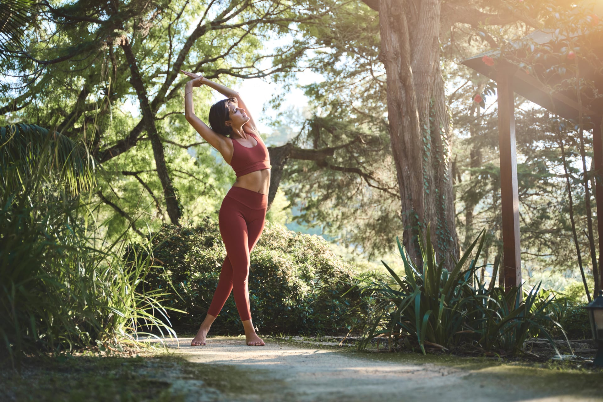 Fit sporty happy young Hispanic woman wearing sportswear meditating doing yoga breathing stretching exercises standing in nature park outdoors in sunny morning. Authentic candid photo.