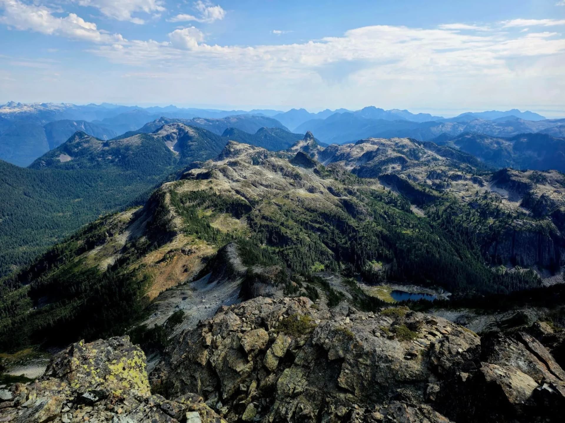 Rocky mountain trail overlook with distant blue peaks and small alpine lake