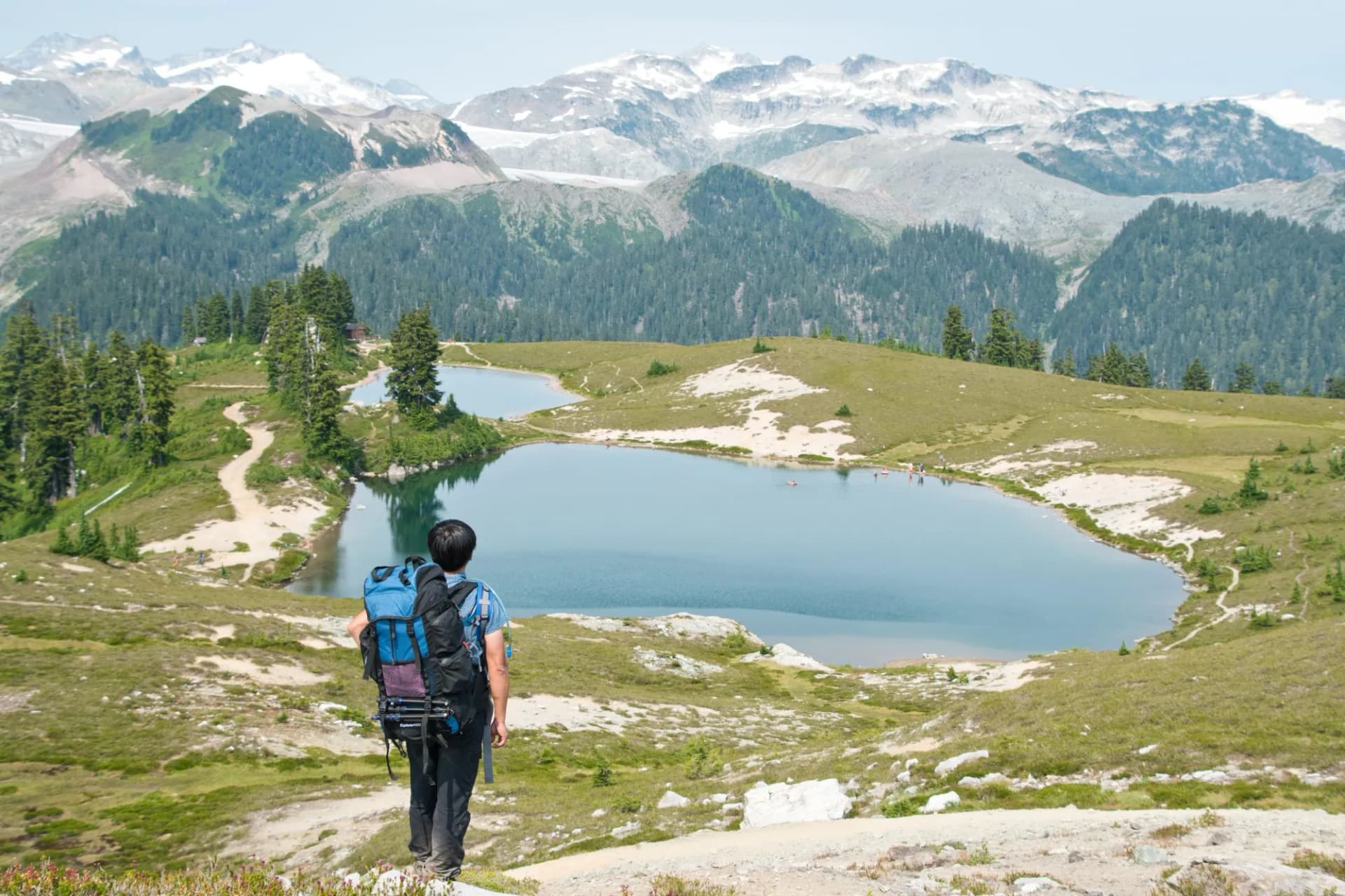 Hiker with backpack overlooking Elfin Lakes and snow-capped mountains in summer.