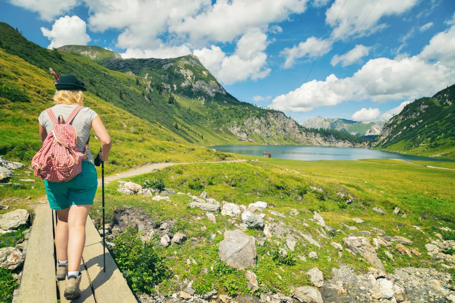 Hiker with backpack walking on wooden path near Tappenkarsee lake surrounded by green mountains