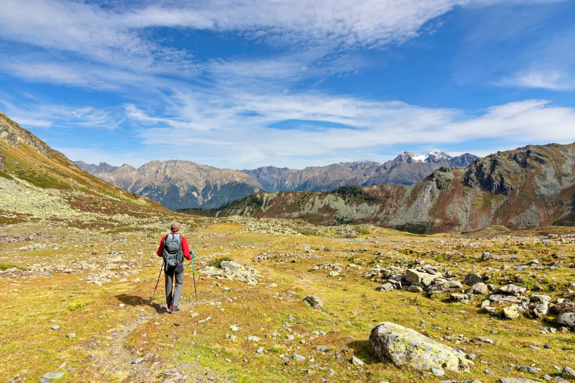 Rear view of a male hiker in autumn walking in the Tyrolean Alps, Austria. Landscape with grass, rocky mountains and blue sky