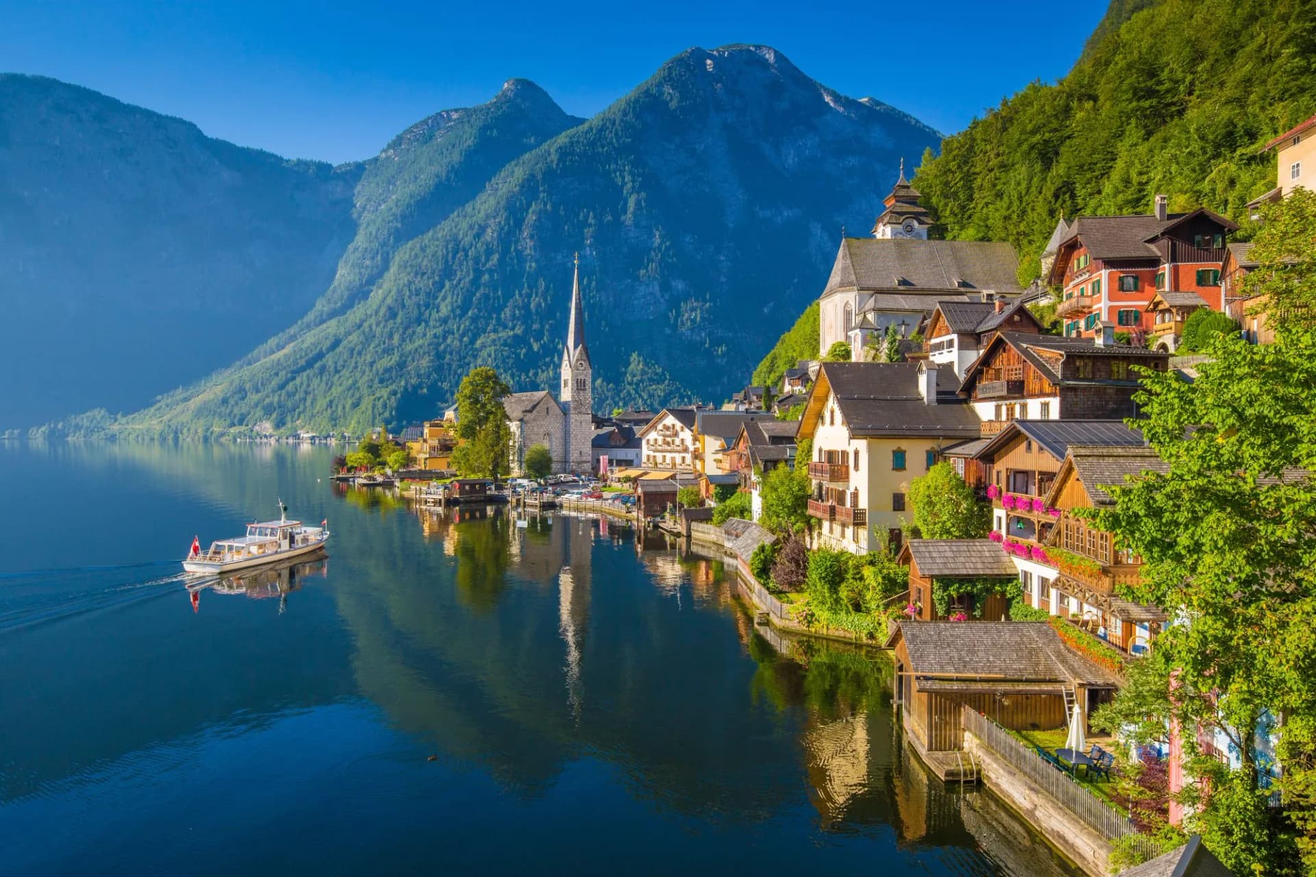 Hallstatt village with church steeple on alpine lake in summer with passenger boat