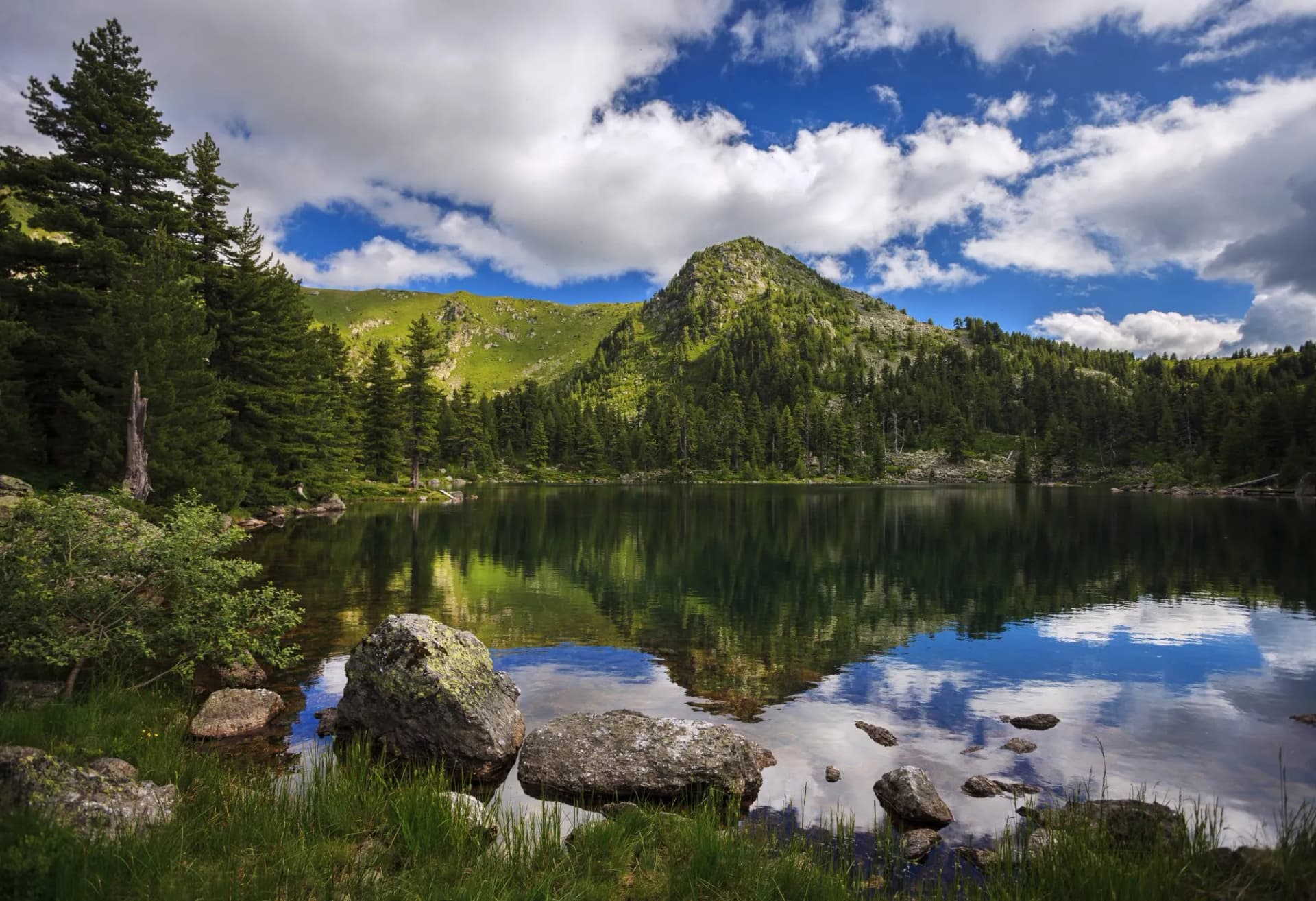 Serene view of Hridsko lake in Prokletije mountains National Park with reflections under a cloudy blue sky.