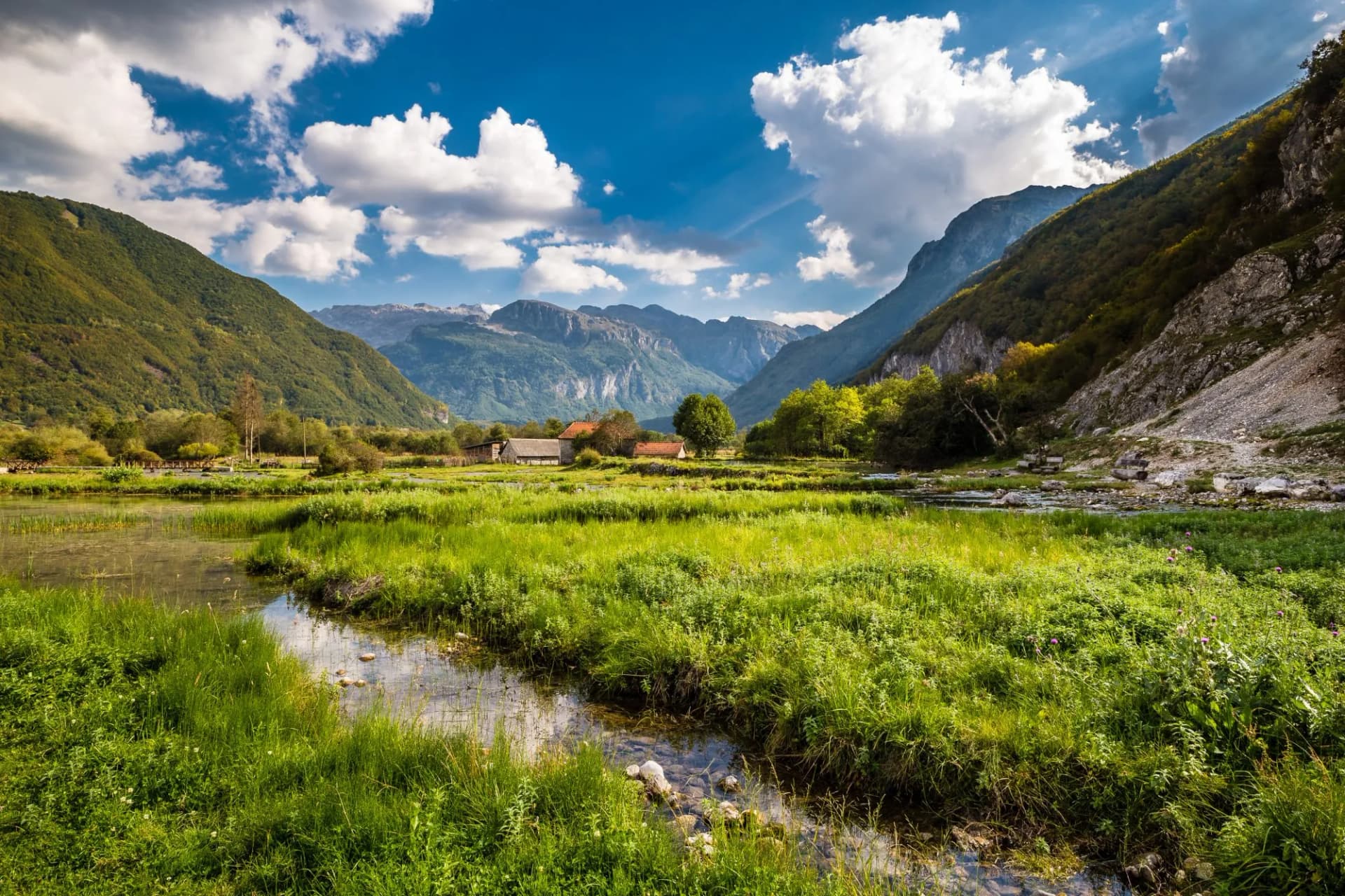 Green spring meadow with stream flowing between mountains near small farm buildings, Ali Pasha Springs.