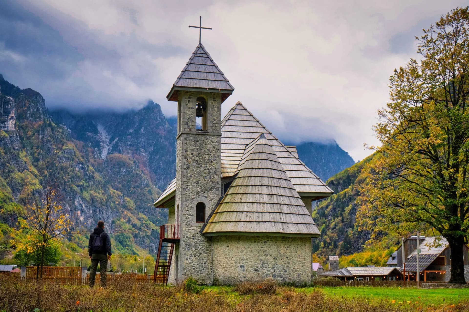Stone church in Thethi National Park with autumn foliage and cloudy mountains.