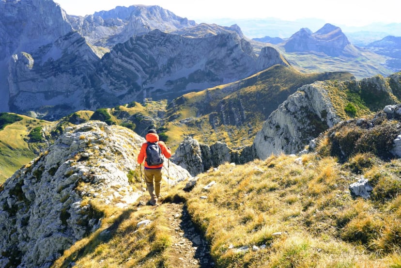 A tourist with a backpack goes down the path in a beautiful area against the backdrop of mountain slopes and peaks. Hiking in Durmitor National Park, Montenegro - trail from the top of Prutas