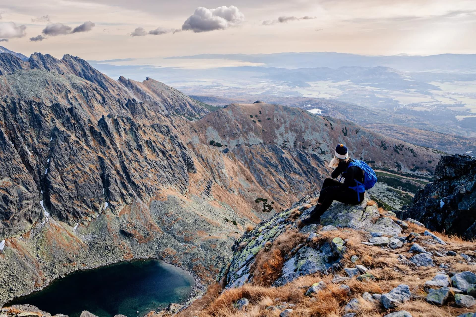 Beautiful blonde woman enjoys the moment while hiking in the Slovak Tatra Mountains on Mount Kryvan. She rests on the route and looks at the lake among the rocky peaks