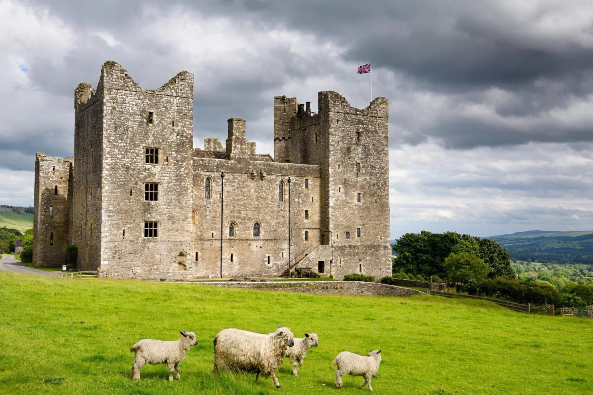 West side of 14th-century Bolton Castle with British flag with clouds and sheep in Wensleydale Yorkshire England