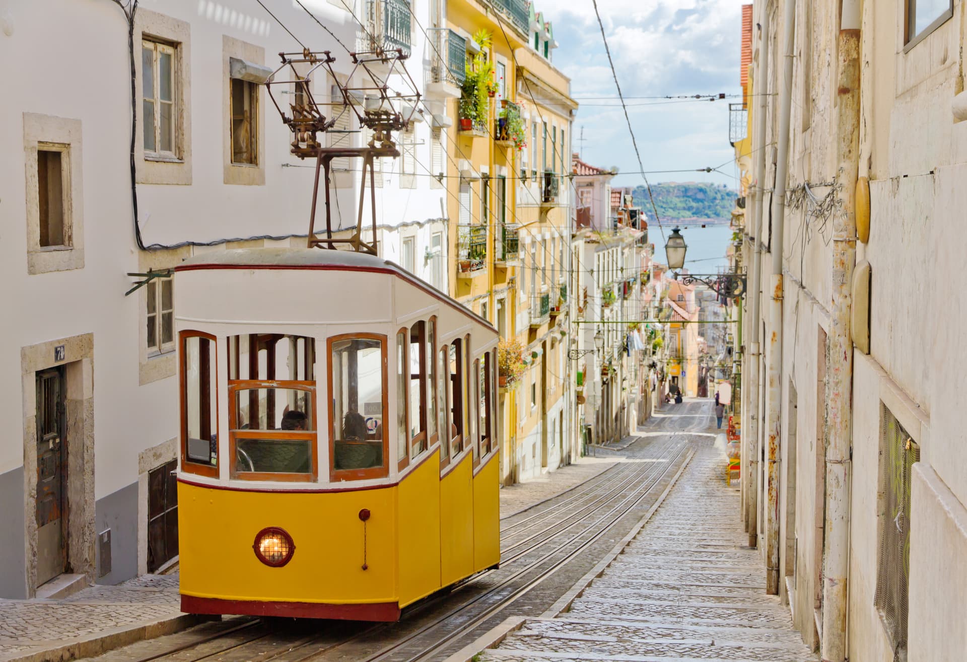 Yellow funicular tram ascending steep cobblestone street between historic buildings in Portugal.
