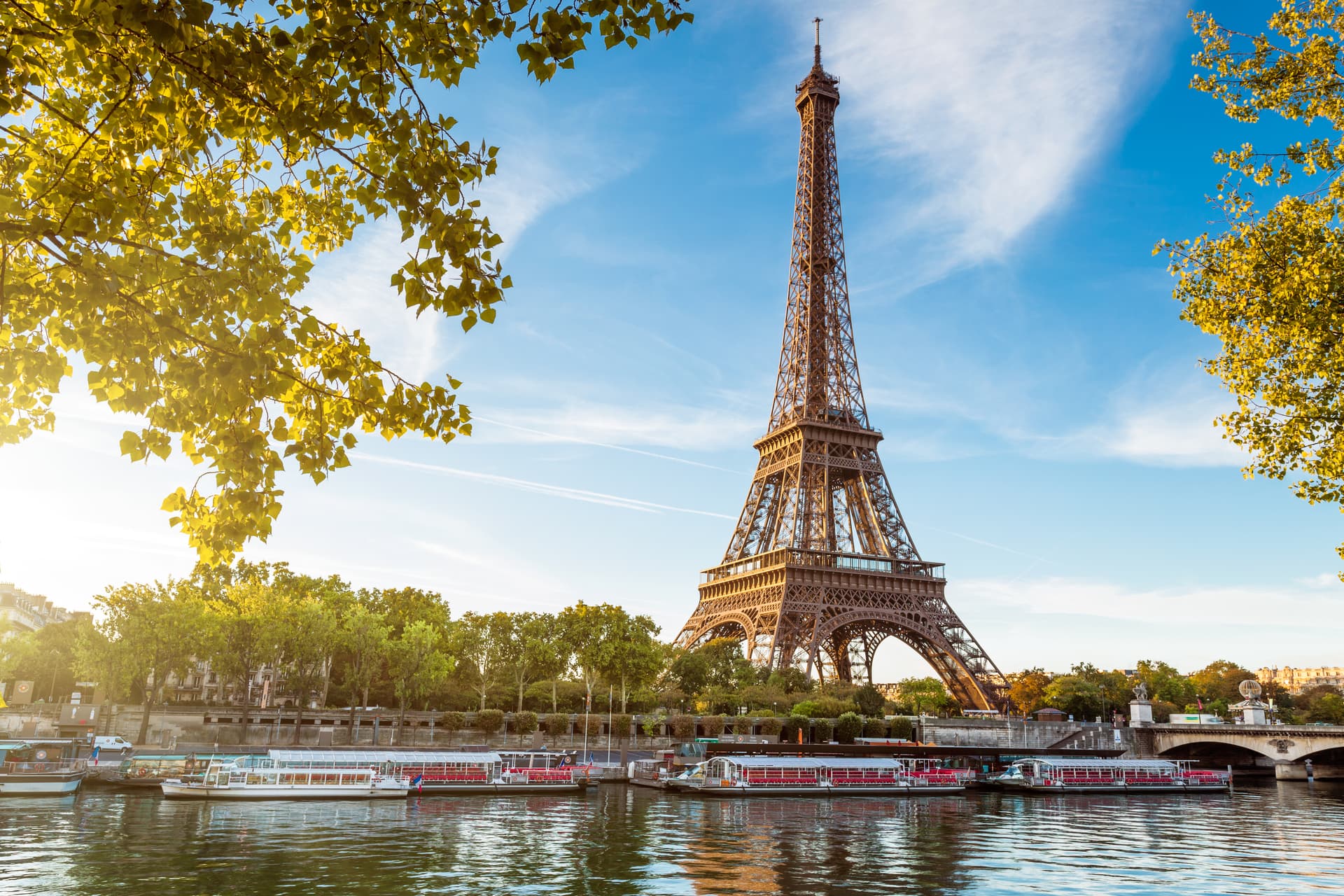 Eiffel Tower over Seine River with tour boats docked, framed by yellowing autumn leaves in Paris.