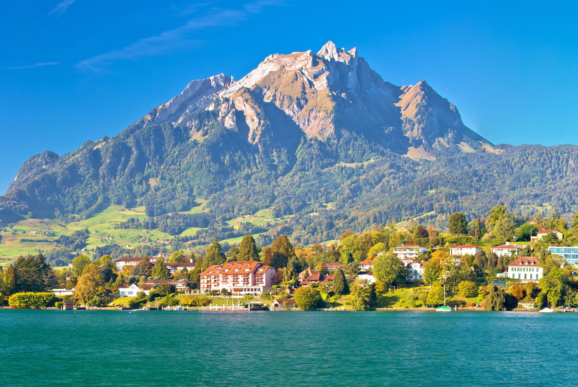 Alpine lake with turquoise water, town, and large mountain under clear blue sky in Switzerland.