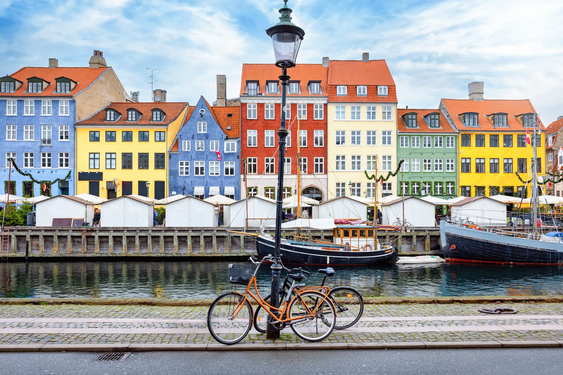 Bicycles parked by lamppost in front of colorful Nyhavn canal houses and moored boats.