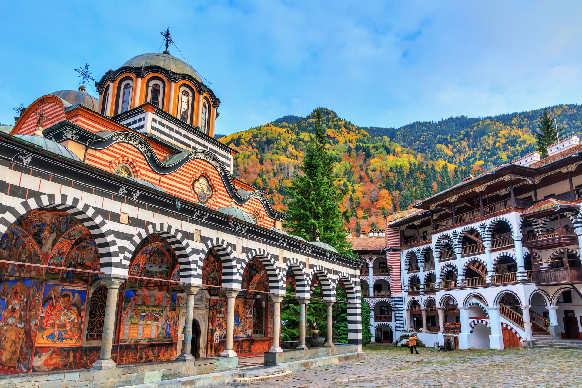 Rila Monastery with colorful frescoes and autumn foliage on mountain backdrop, Bulgaria.