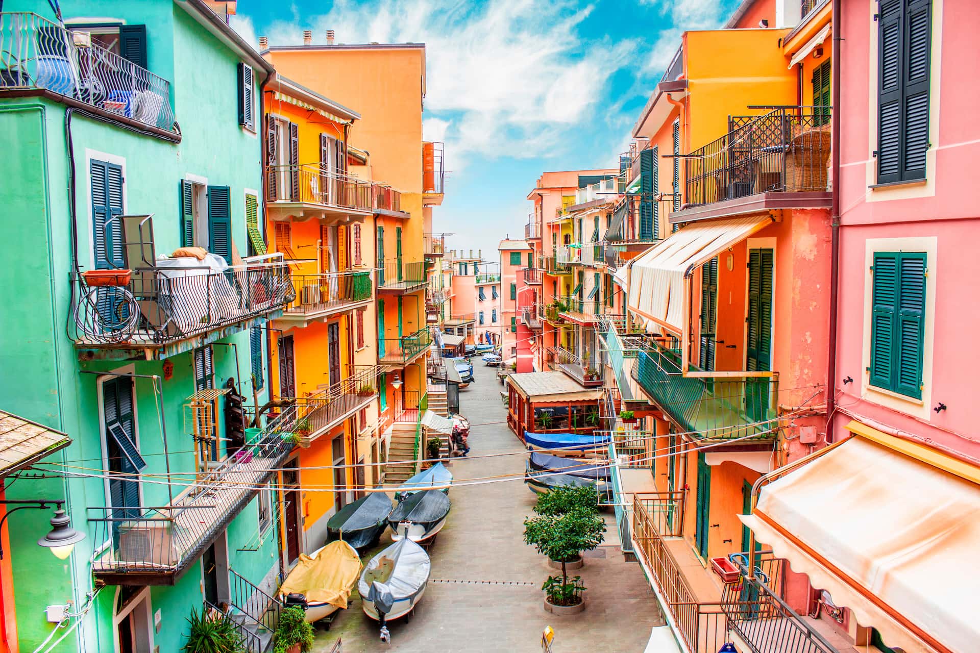 Colorful coastal village street with stacked apartment buildings and boats parked on the pavement.