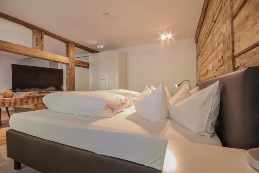 Bedroom with white bedding, exposed wood beams, and rustic wood accent wall