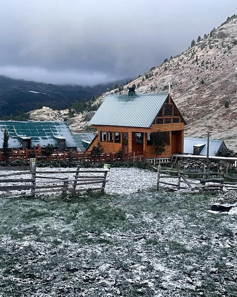 Wooden cabin with green roof in snowy mountain setting under cloudy sky