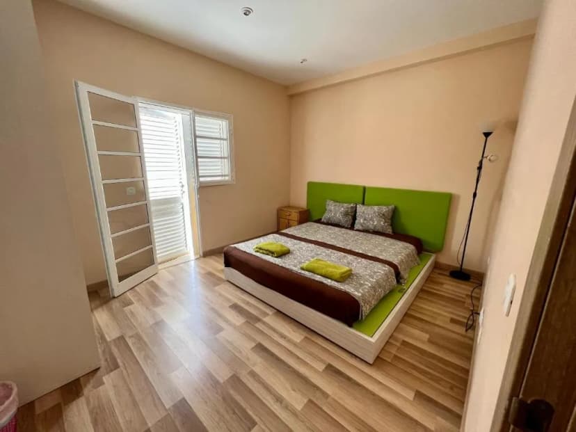 Double bed with green headboard in simple B&B room with wood floor and balcony access.
