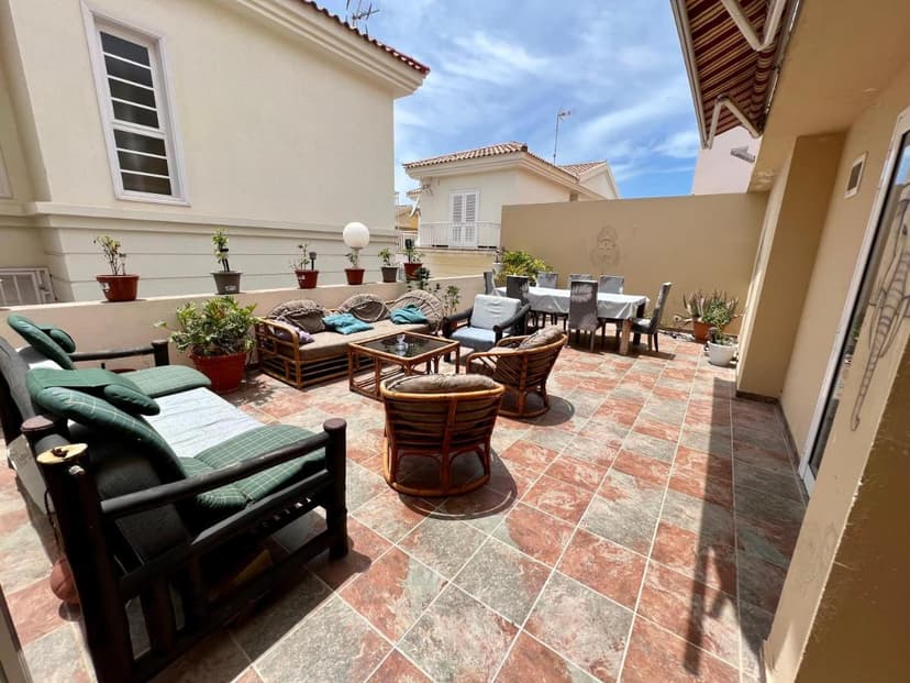 Rooftop terrace with outdoor seating, dining table, and potted plants under a sunny sky.