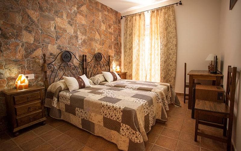 Twin beds with patchwork quilts in a room featuring a rustic stone accent wall and terracotta floor.