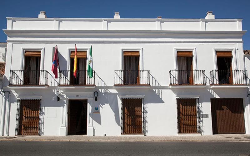 White rural house with balconies flying Spanish and Andalusian flags under blue sky
