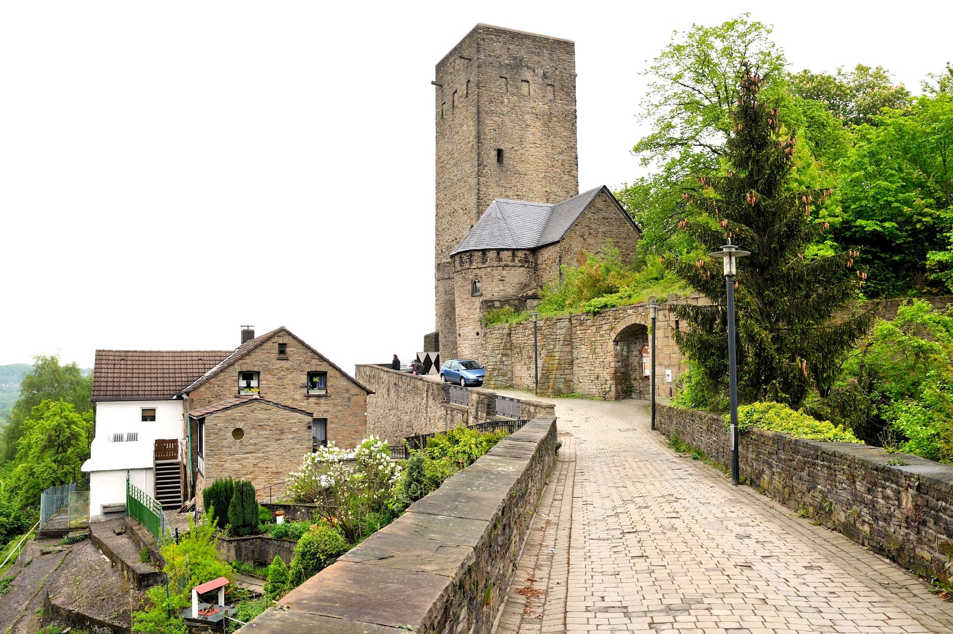 Stone tower and historic buildings along a cobblestone path near lush green trees at Blankenburg Castle.