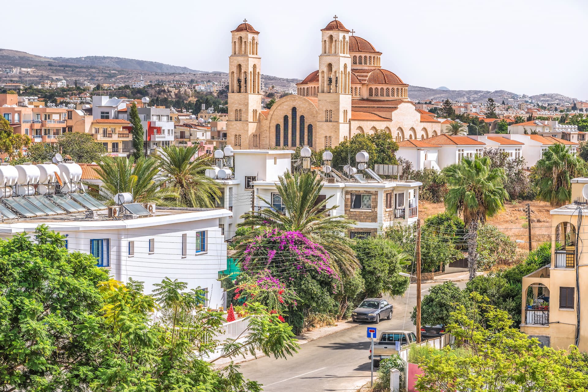 Large Orthodox church overlooking Paphos town with palm trees and sun-heated water tanks.