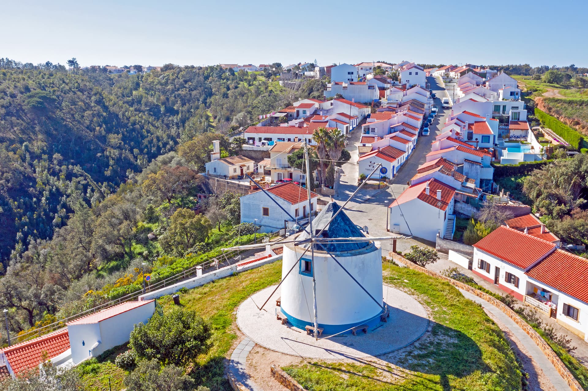Windmill in Odeceixe, Portugal, overlooking white houses with red roofs and green hillside.