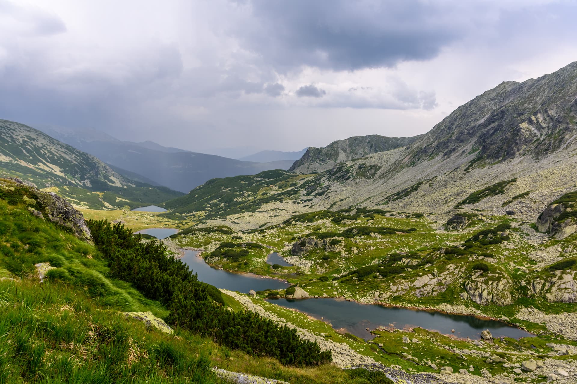 Alpine lakes nestled in rocky valleys with green slopes under a stormy sky in Retezat.