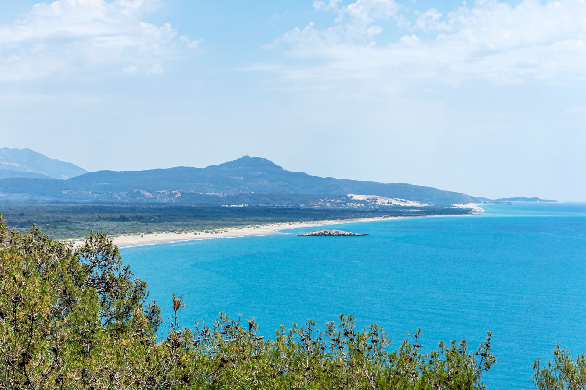 View of Karadere Beach with turquoise sea, sandy coastline, and distant blue mountains.