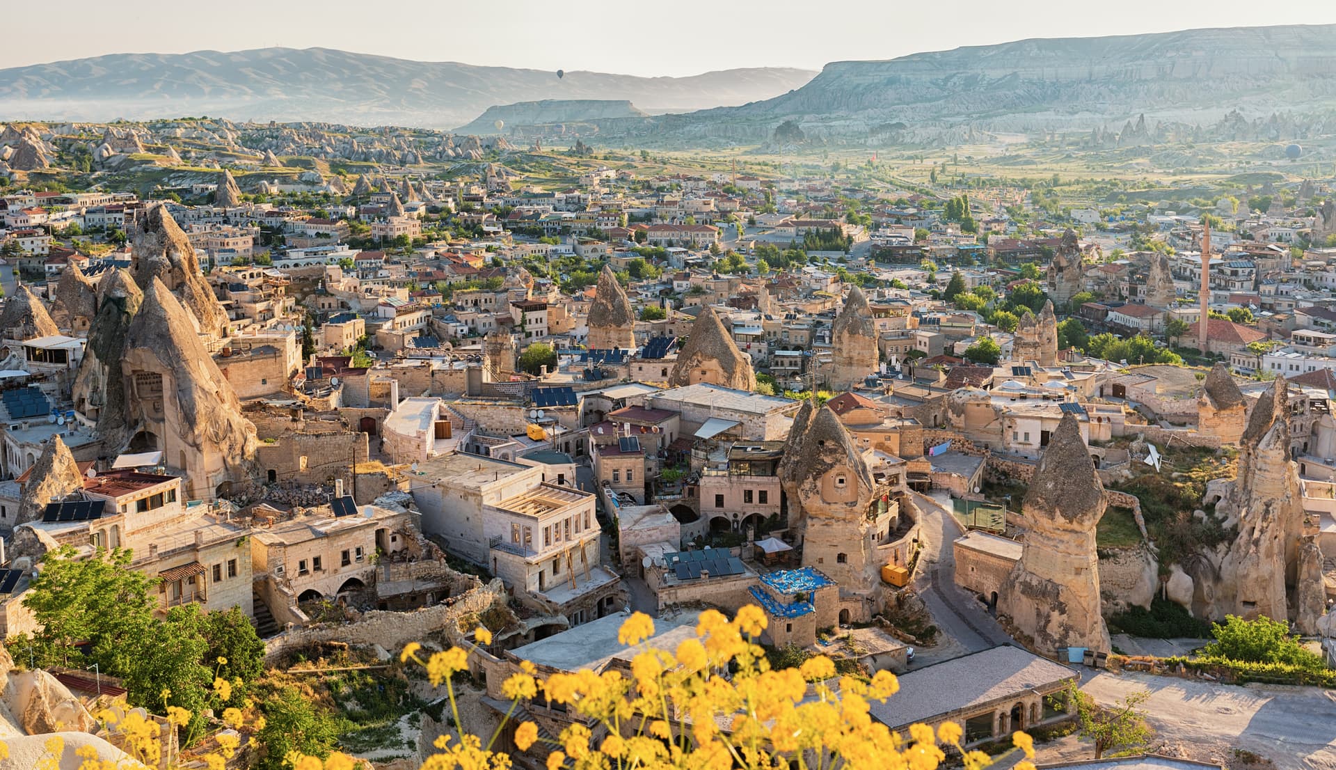 Göreme town with cave dwellings, fairy chimneys, and hot air balloons over Cappadocia valleys.