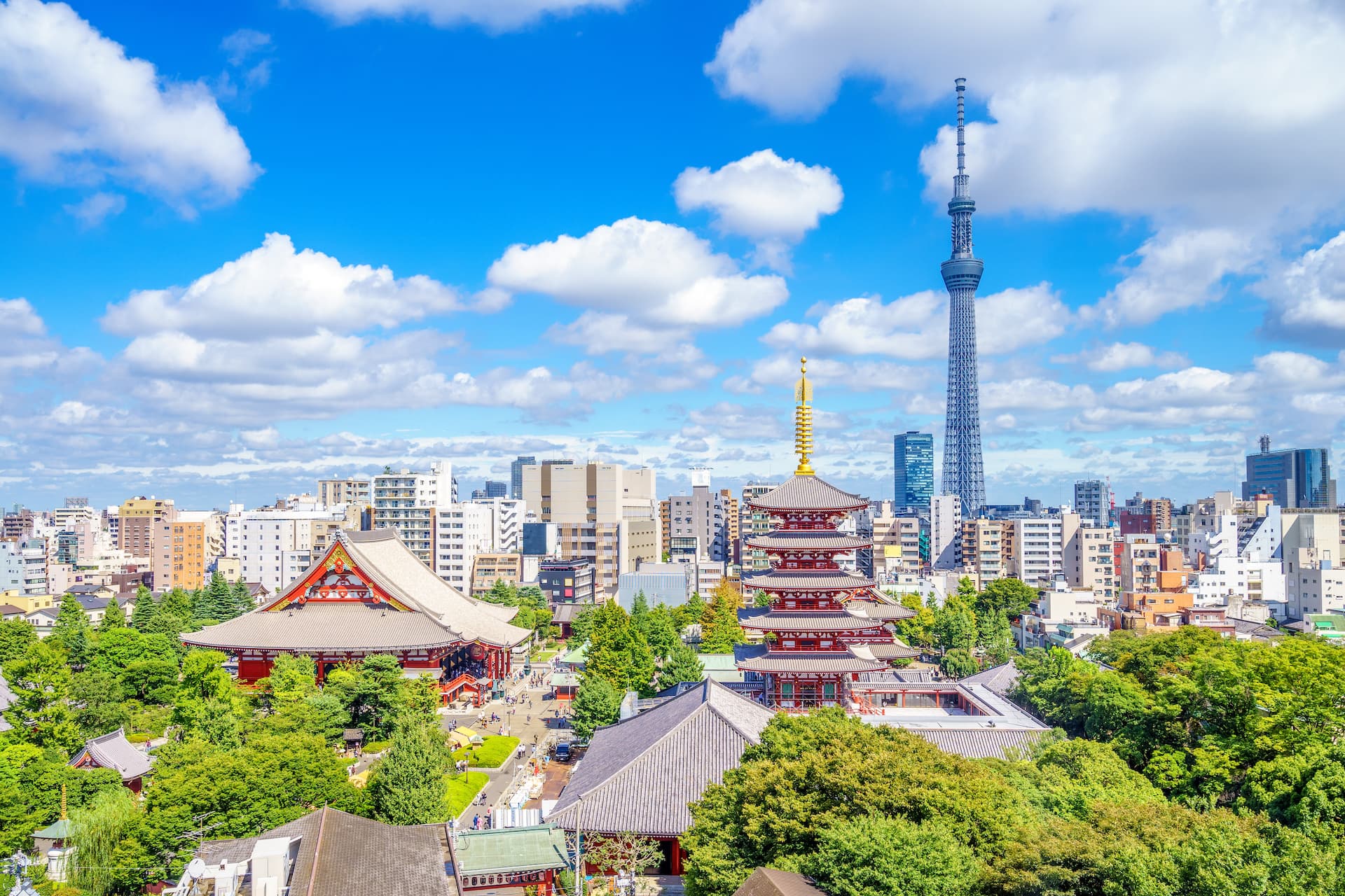 Pagoda and temple complex surrounded by green trees with Tokyo Skytree in the background.