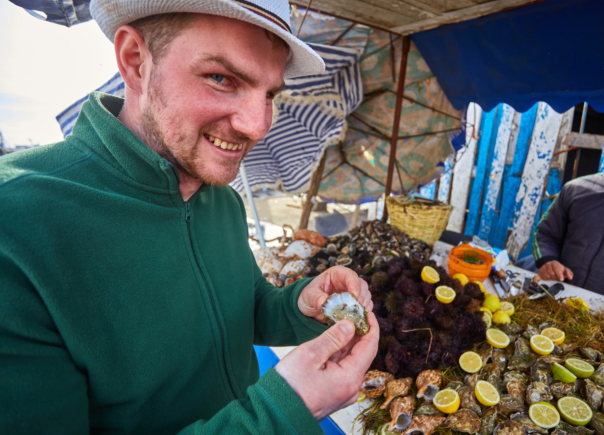 Man trying an oyster at a seafood stall in the port of Essaouira, Morocco.