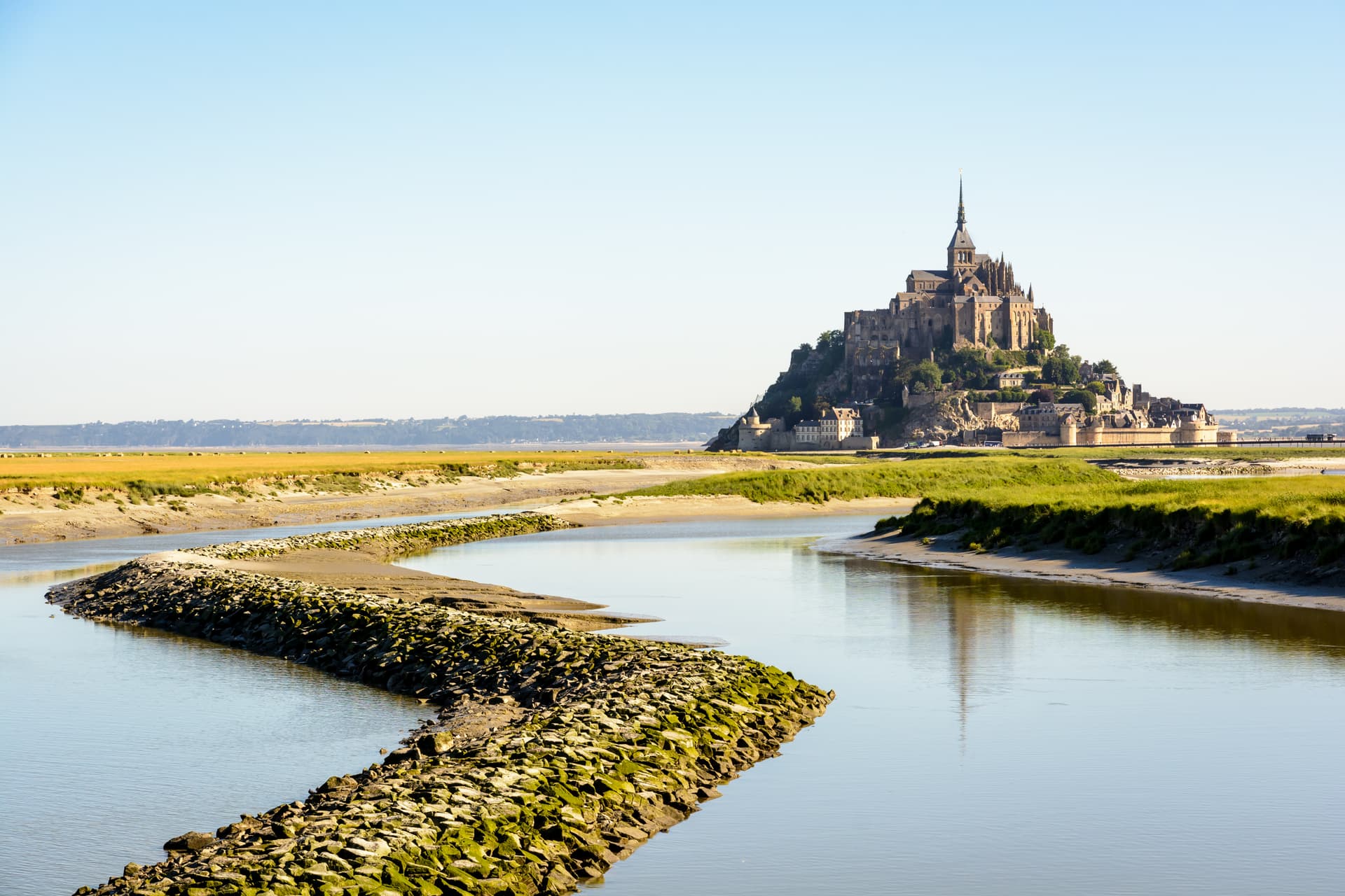 Mont Saint-Michel tidal island in France seen across marshland with a stone-lined channel.