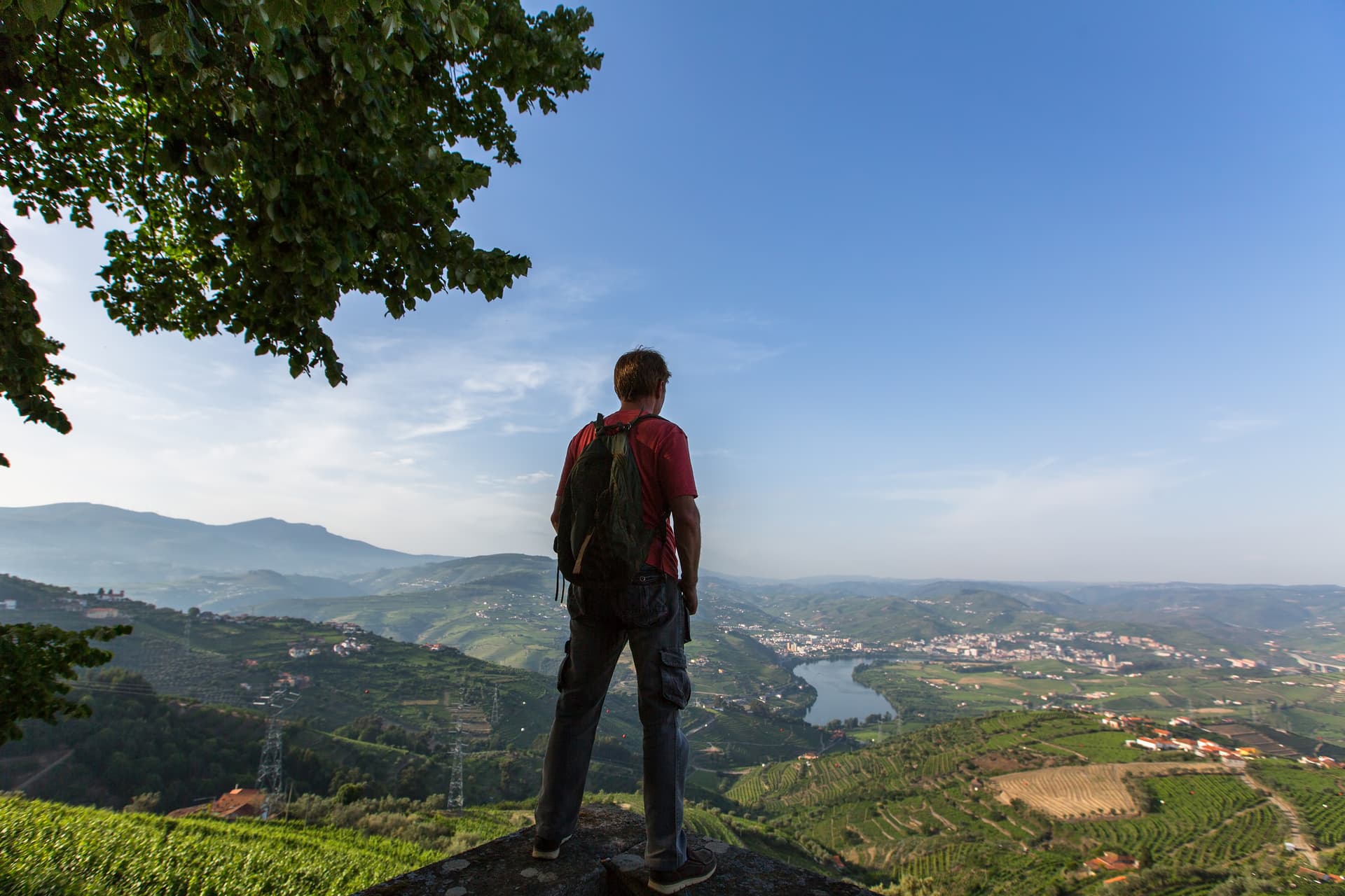 Hiker with backpack enjoying view of Douro Valley, Portugal, with terraced vineyards and river.