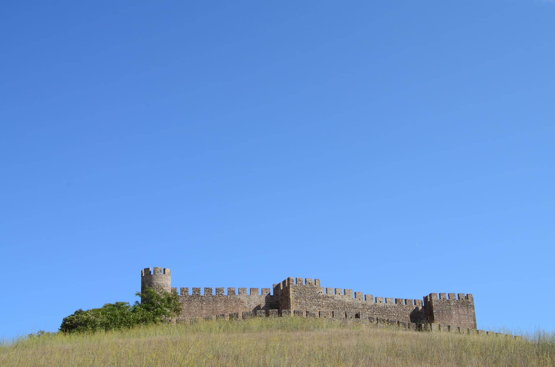 Castelo de Santiago do Cacém stone fortress ruins atop a grassy hill under a clear blue sky.