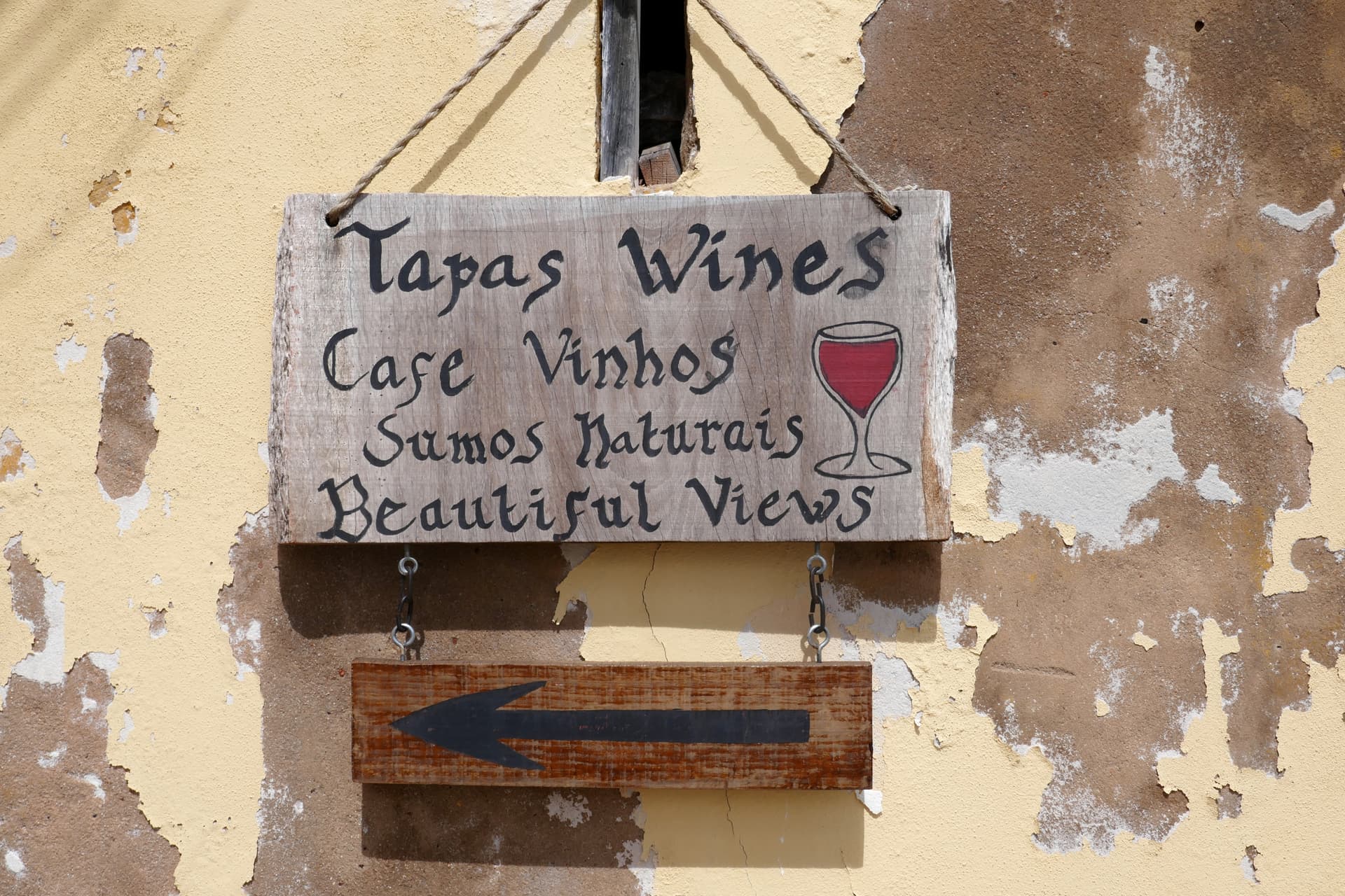 Wooden sign for Tapas Wines Cafe pointing left, hanging on a peeling yellow stucco wall.