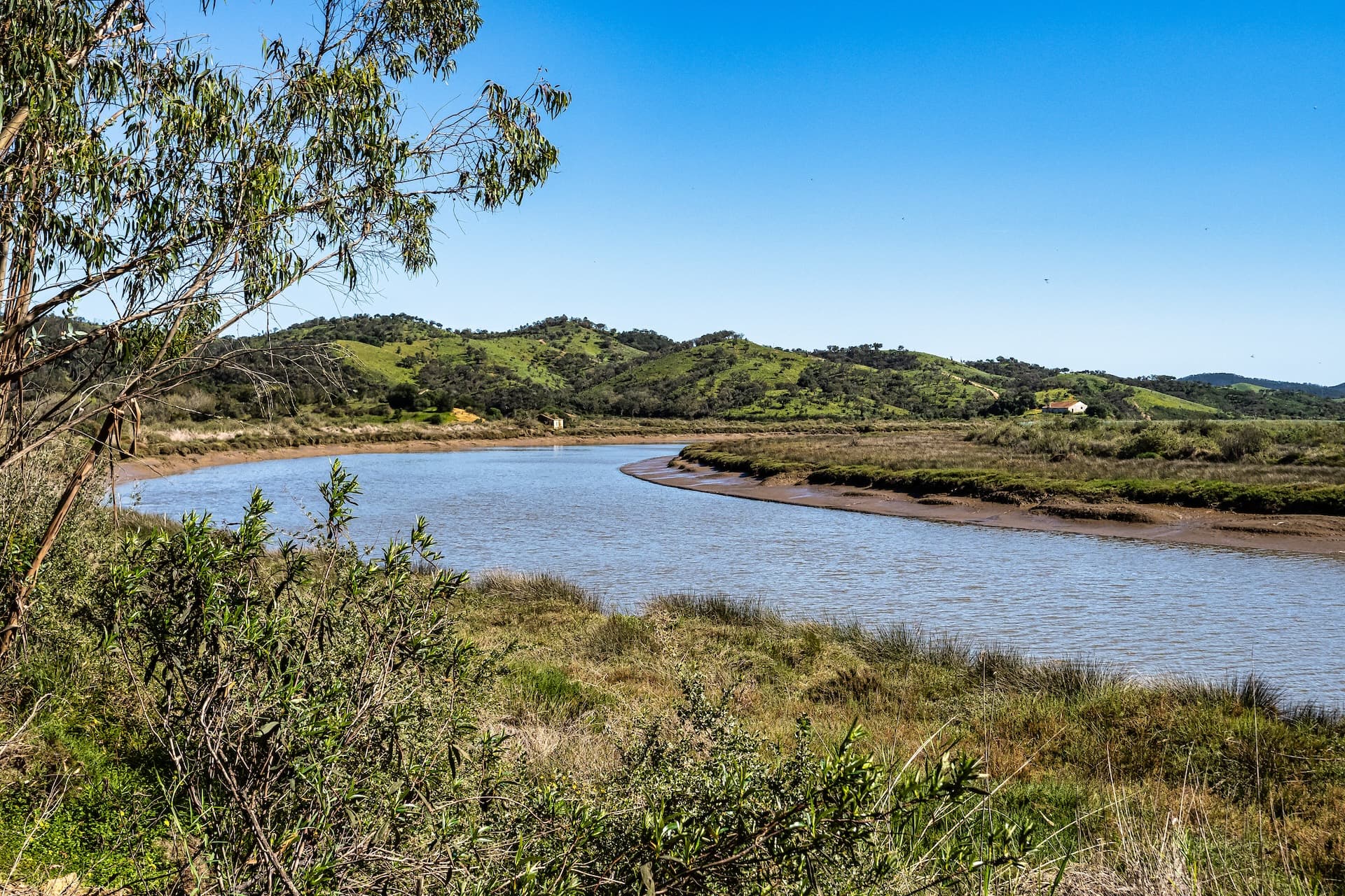 Walking the Rota Vicentina along the River Mira with green hills under a clear blue sky.