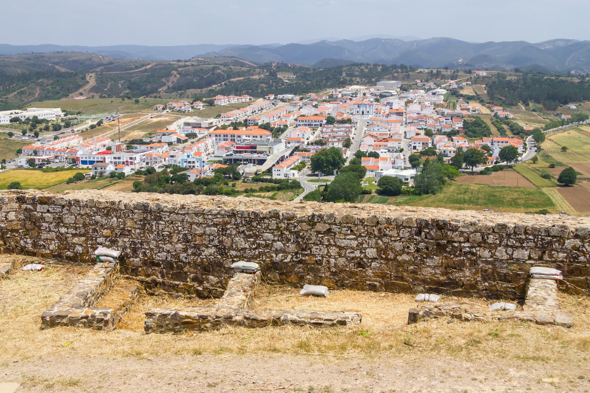 Stone castle ruins overlook Aljezur village with white houses, a church, and green hills.
