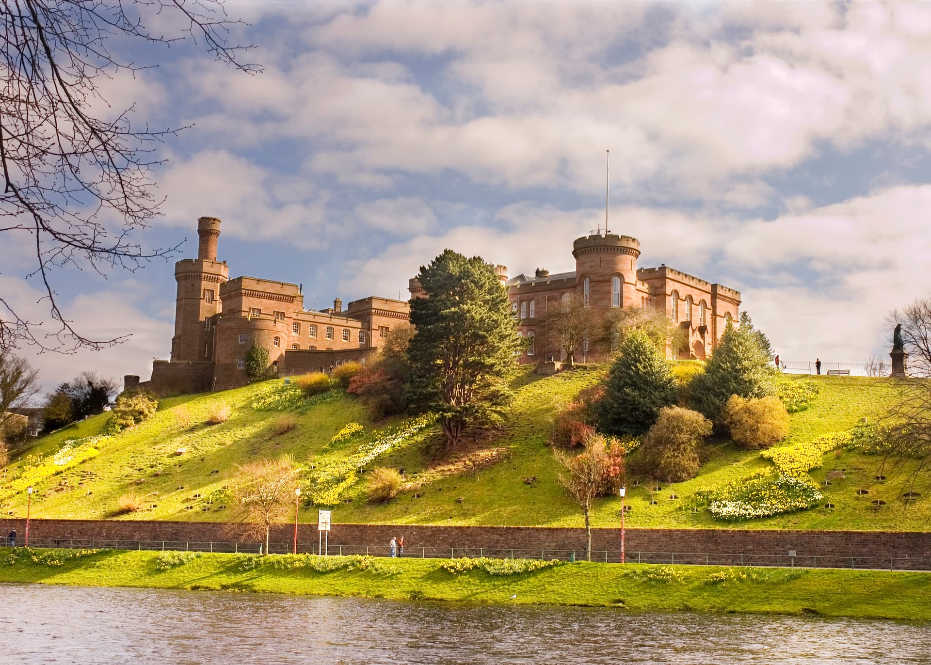 Inverness Castle on grassy hill with daffodils above river under cloudy sky