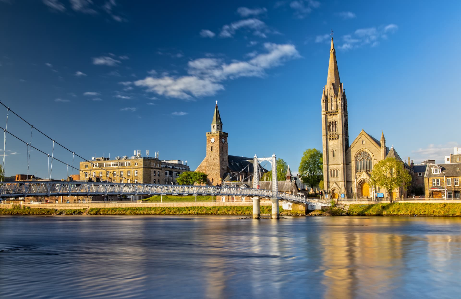 Suspension bridge over river with church and clock tower in Inverness, Scotland