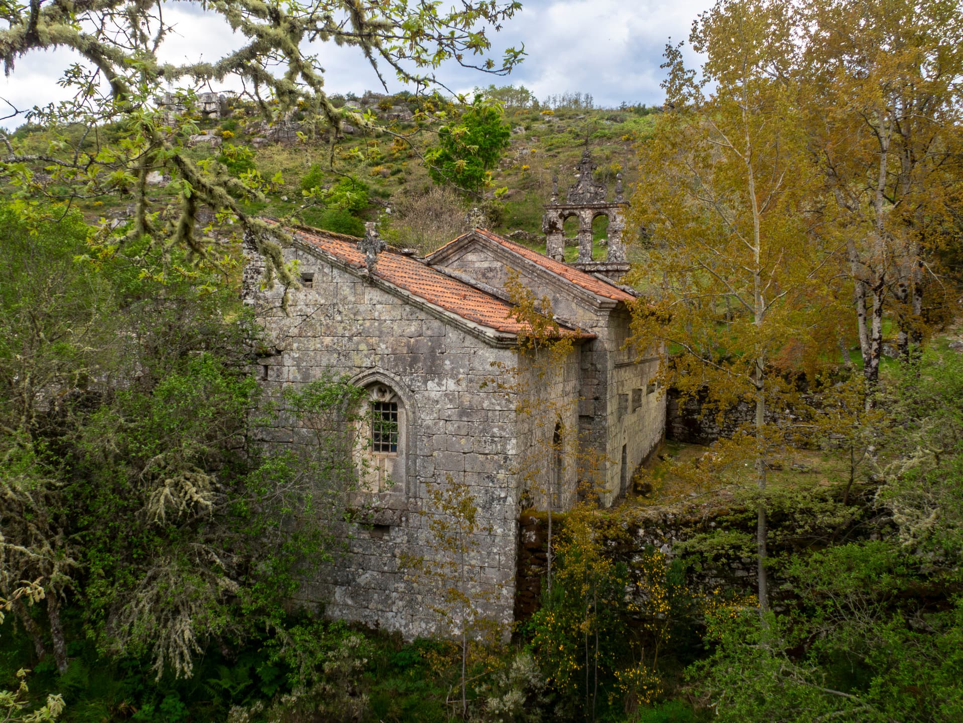 Stone Monastery of Santa Maria das Júnias surrounded by lush green and yellow foliage in Montalegre, Portugal.