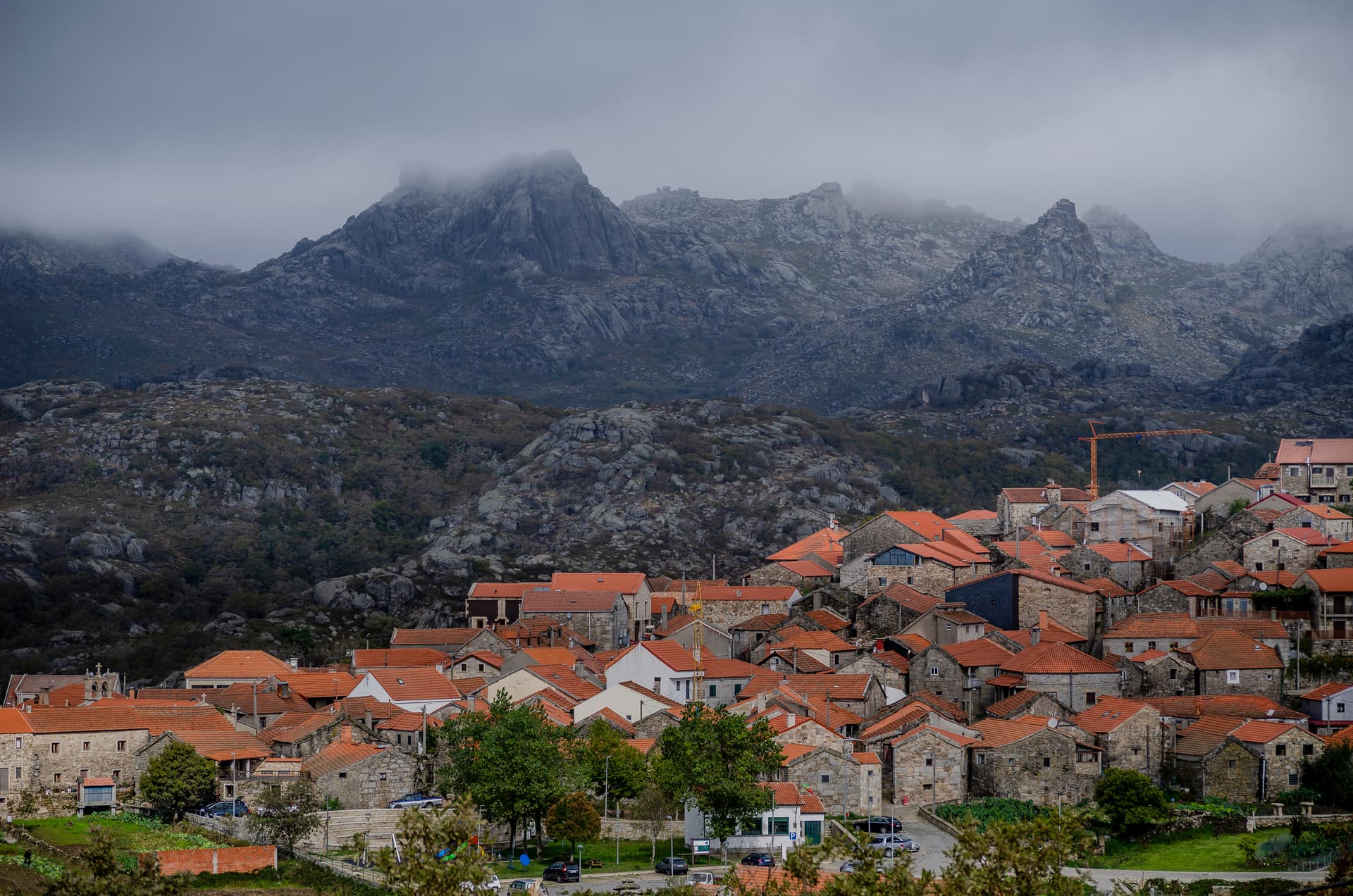 Village of Pitoes das Junias with stone houses and orange roofs below foggy, rocky mountains in Peneda-Geres National Park.