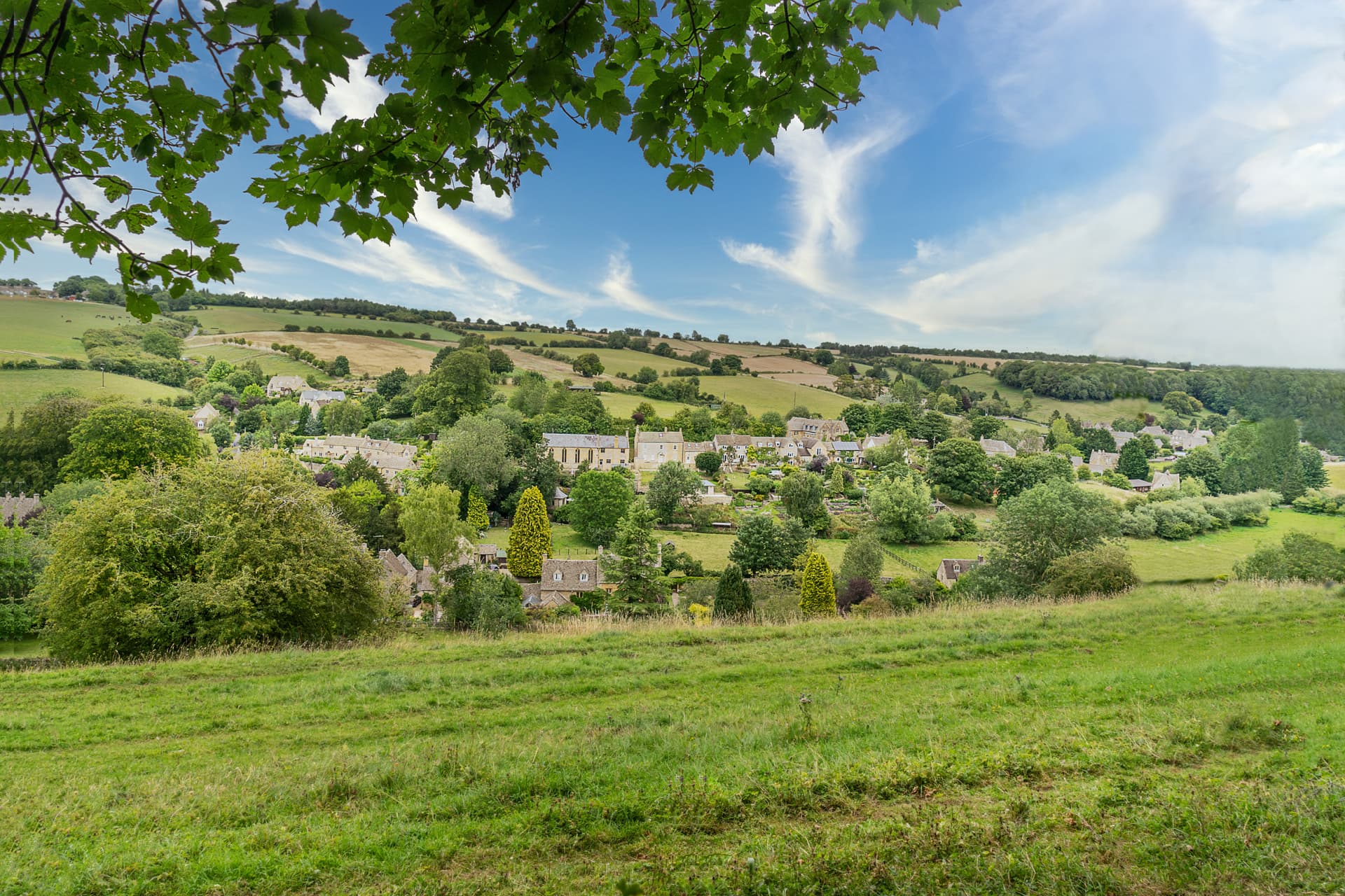 English stone cottage village nestled in rolling green countryside under a blue sky.