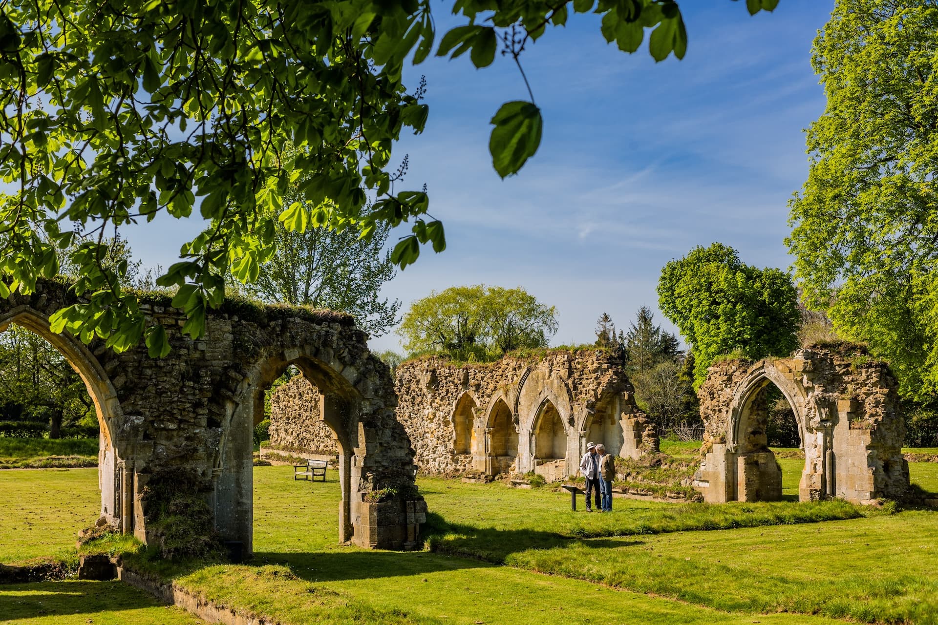Ruins of Hailes Abbey with stone arches on a sunny day, framed by green leaves.