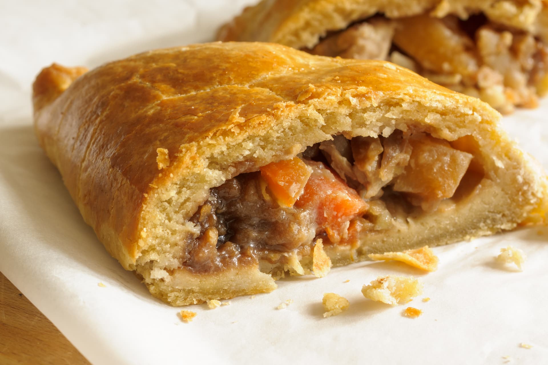 Golden baked pastry filled with meat and carrots, served on white paper.