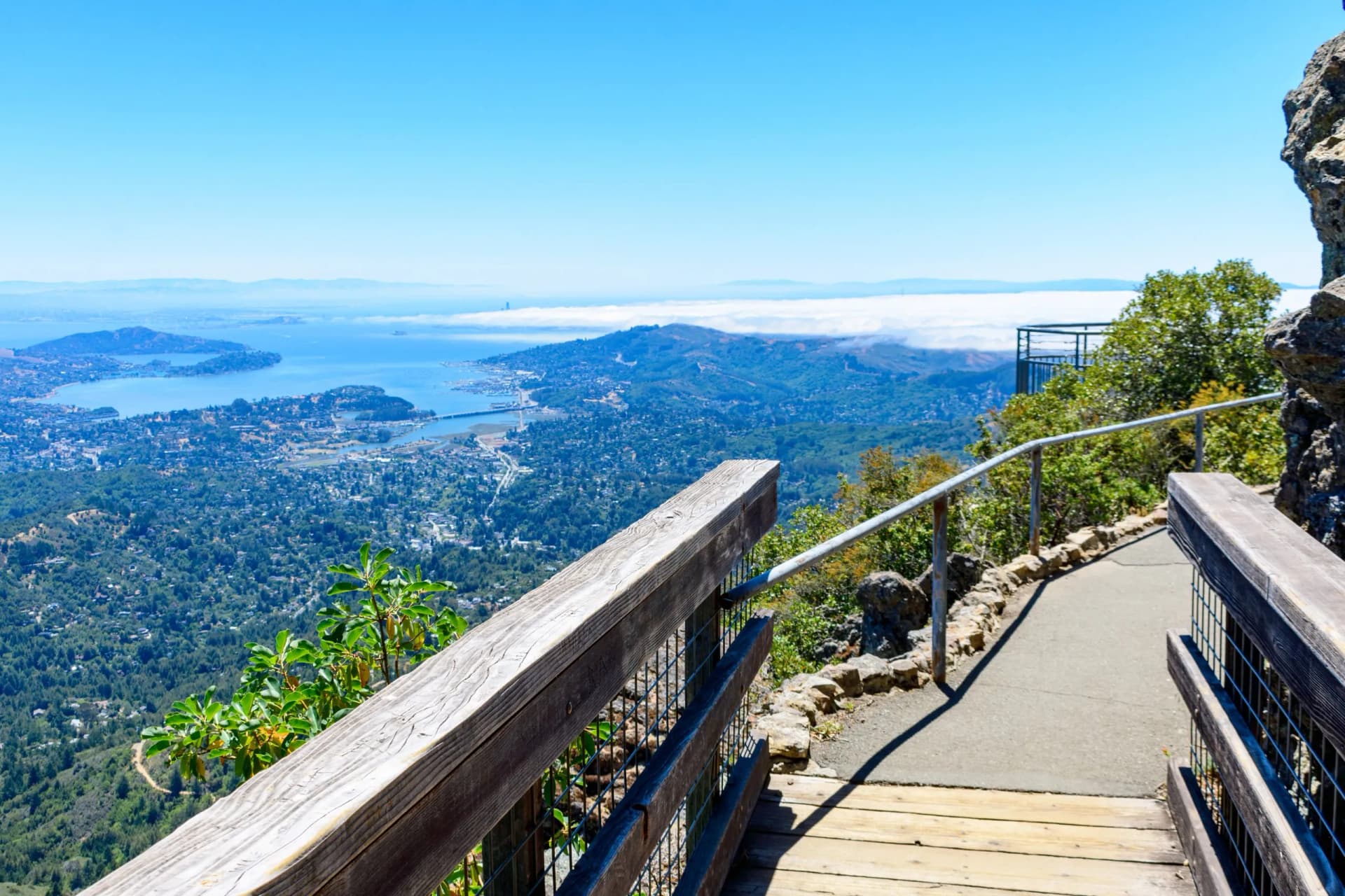 Hiking trail overlook with wooden railing above San Francisco Bay Area and fog layer.