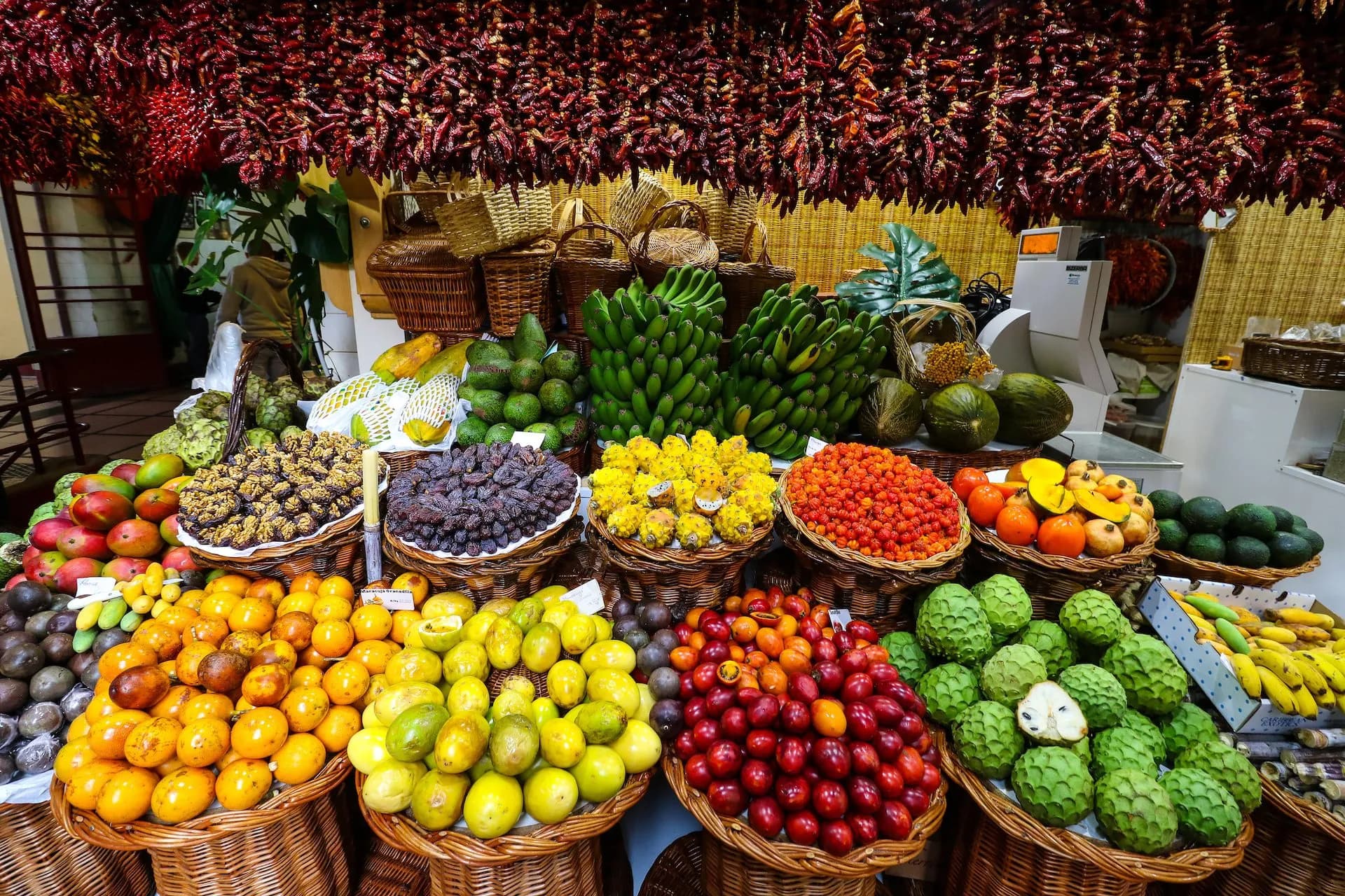 Abundant fresh fruit display with hanging red peppers at Mercado dos Lavradores.