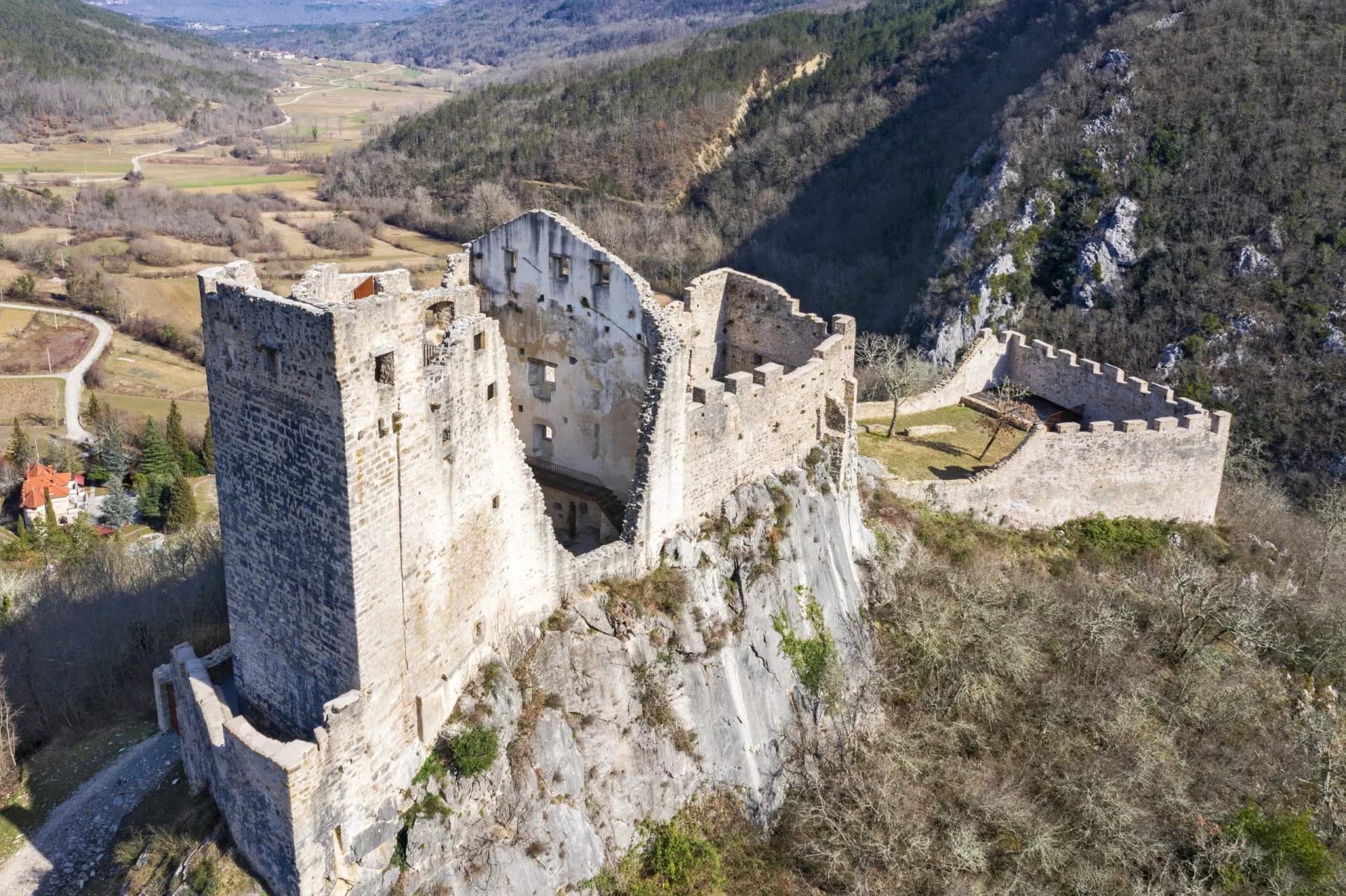 Ruins of Istria Castle perched on a rocky cliff overlooking a valley with bare winter trees.