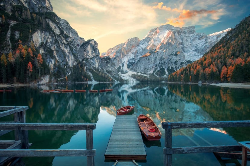 Wooden rowboats docked at a pier on Lago di Braies with reflections of autumn mountains.